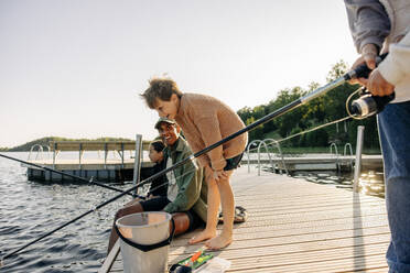 Father and son fishing in river while sitting on boardwalk stock photo