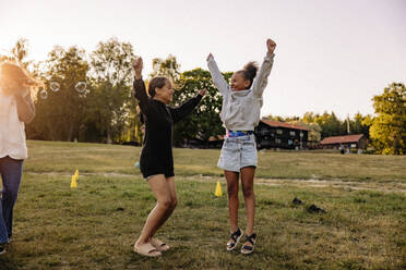 Cheerful girls jumping with arms raised on grass while playing in playground - MASF39506