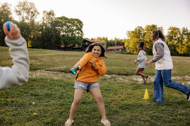 Happy girl splashing water while playing with friends on grass in playground at summer camp - MASF39527