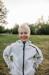 Portrait of smiling boy standing with hands in pockets at playground - MASF39548