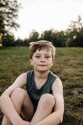 Portrait of boy sitting on grass in playground - MASF39550