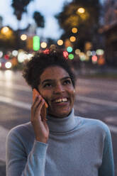 Glückliche junge Frau, die in der Abenddämmerung mit ihrem Smartphone telefoniert - JOSEF20967