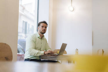 Contemplative businessman sitting with laptop in cafe - JOSEF20990