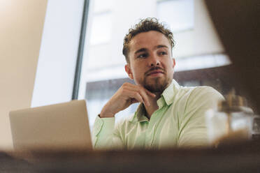 Young businessman with laptop sitting in cafe - JOSEF20992