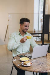 Happy businessman with coffee cup working on laptop at table in cafe - JOSEF20997