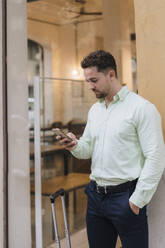 Junger Geschäftsmann benutzt sein Smartphone vor einem Cafe - JOSEF21005