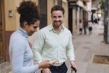 Happy businessman with colleague using smart phone on footpath - JOSEF21006