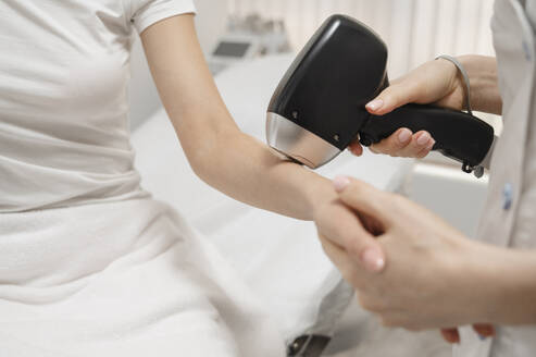 Kosmetikerin entfernt Haare mit Laser an der Hand einer Frau - ALKF00600