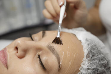 Dermatologist applying chemical peel with brush on woman's face - ALKF00611