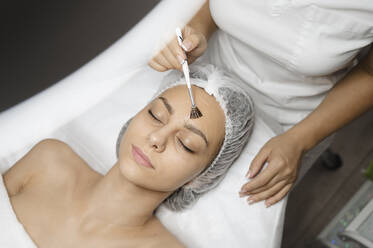 Dermatologe trägt chemisches Peeling mit Pinsel auf das Gesicht einer Frau auf - ALKF00612