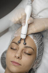 Hände eines Dermatologen massieren mit einem Gerät die Stirn einer Frau - ALKF00622