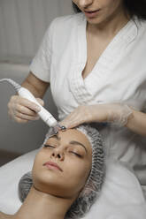 Junger Dermatologe massiert mit einem Gerät die Stirn einer Frau - ALKF00623