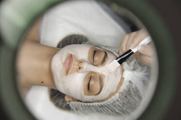 Hand of beautician applying skincare mask with brush on woman's face - ALKF00638