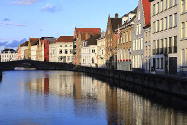 Belgien, Westflandern, Brügge, Reihe von Stadthäusern am Flussufer mit Bogenbrücke im Hintergrund - JTF02380