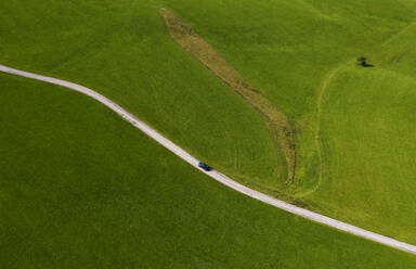 Austria, Upper Austria, Hausruckviertel, Drone view of car driving along dirt road cutting through green field - WWF06438