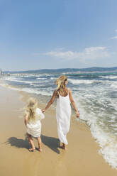 Mother and daughter walking on coastline at beach - SIF00859