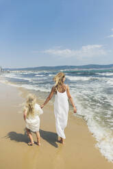 Mutter und Tochter spazieren an der Küstenlinie am Strand - SIF00859