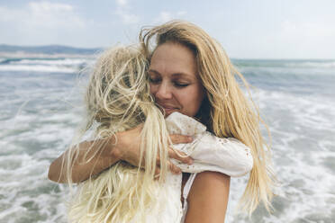 Lächelnde Mutter, die ihre Tochter am Strand umarmt - SIF00864