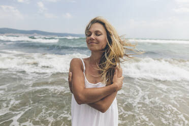 Smiling woman hugging self at beach - SIF00874