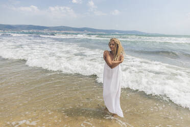 Smiling woman hugging self on coastline at beach - SIF00875