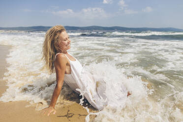 Glückliche Frau sitzt im Wasser am Strand - SIF00876