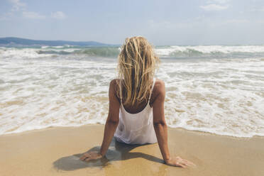 Blonde Frau sitzt auf Sand am Strand - SIF00878