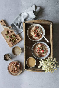 Studioaufnahme eines Holztabletts mit Schalen mit veganem Porridge, Wildblumen und Rhabarberkompott - EVGF04386