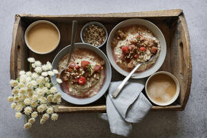 Studioaufnahme eines Holztabletts mit Schalen mit veganem Porridge, Wildblumen und Rhabarberkompott - EVGF04387