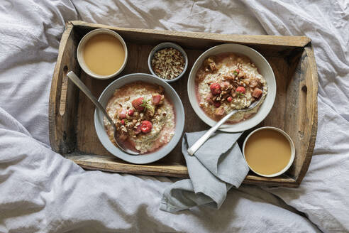 Holztablett mit Schalen mit veganem Porridge und Rhabarberkompott auf dem Bett liegend - EVGF04388