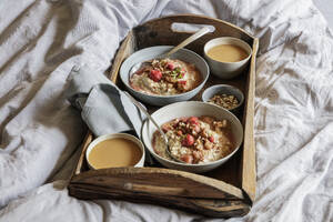 Holztablett mit Schalen mit veganem Porridge und Rhabarberkompott auf dem Bett liegend - EVGF04389