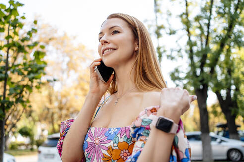 Lächelnde Frau, die auf der Straße mit einem Mobiltelefon spricht - NLAF00098