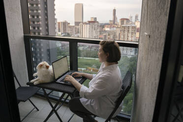 Young freelancer using laptop with cat sitting on table - YBF00229