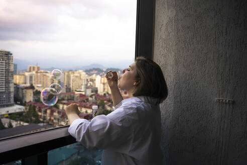 Young woman blowing bubbles on balcony - YBF00233
