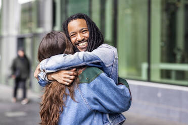 Cheerful man hugging woman at footpath in front of building - WPEF07672