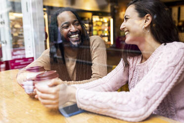 Glückliches gemischtrassiges Paar sitzt mit Kaffeetassen in einem Cafe - WPEF07675