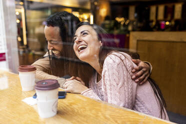 Fröhlicher Mann und Frau mit Kaffeetassen sitzen am Tisch in einem Café - WPEF07678