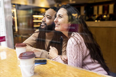 Lächelnder Mann und lächelnde Frau mit Kaffeetassen sitzen am Tisch in einem Café - WPEF07679