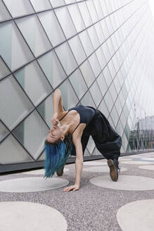 Flexible Tänzerin, die sich vor einem modernen Gebäude nach hinten beugt - MMPF00875