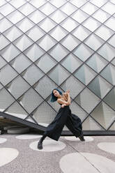 Junge Frau tanzt vor einem modernen Gebäude - MMPF00878
