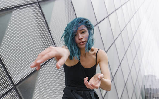 Young dancer with blue dyed hair dancing in front of modern building - MMPF00886