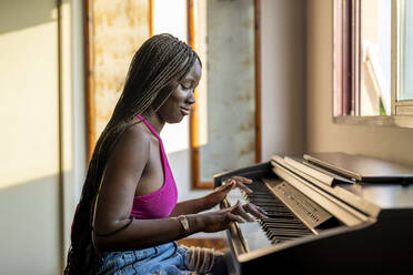 Smiling young woman playing piano at home - DLTSF03602