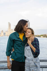 Man kissing woman standing in front of sea - IKF01218