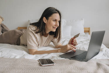 Glückliche Frau, die eine Kreditkarte zum Einkaufen am Laptop zu Hause benutzt - EVKF00057