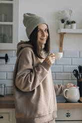 Smiling woman holding tea cup in kitchen - EVKF00082