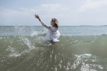 Frau mit erhobener Hand spritzt Wasser im Meer - SIF00895
