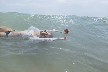 Woman wearing bikini floating on water in sea - SIF00899