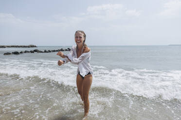 Glückliche Frau im Wasser stehend und lachend am Strand - SIF00904