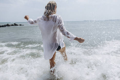 Unbekümmerte Frau, die am Strand im Wasser plantscht - SIF00905