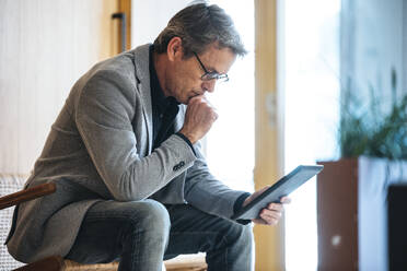 Businessman with hand on chin using tablet PC in office - JSRF02577