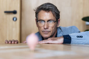 Businessman looking at spinning top at desk - JSRF02590